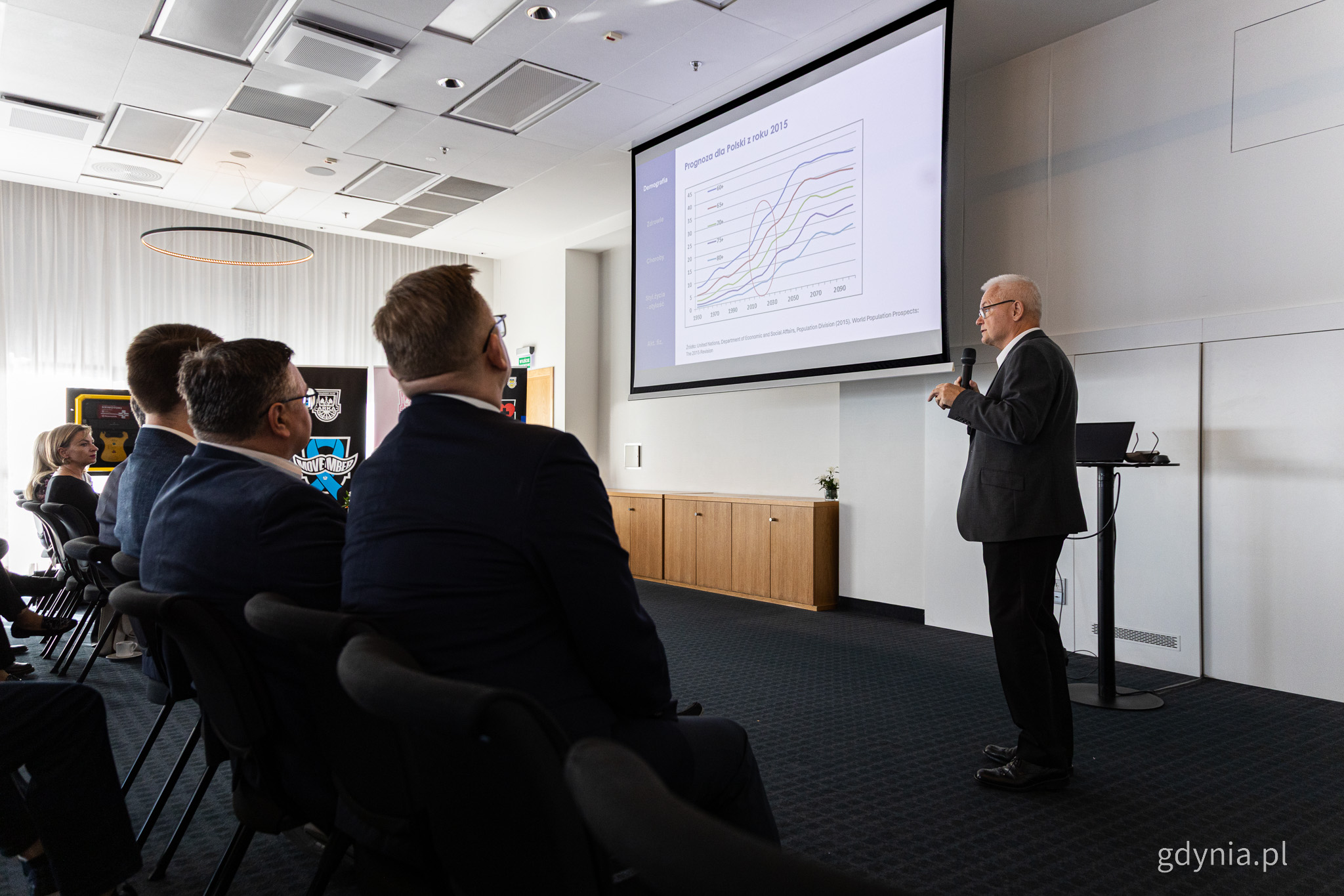 Sala konferencyjna, Tomasz Zdrojewski wyświetla prezentację i m&oacute;wi do mikrofonu