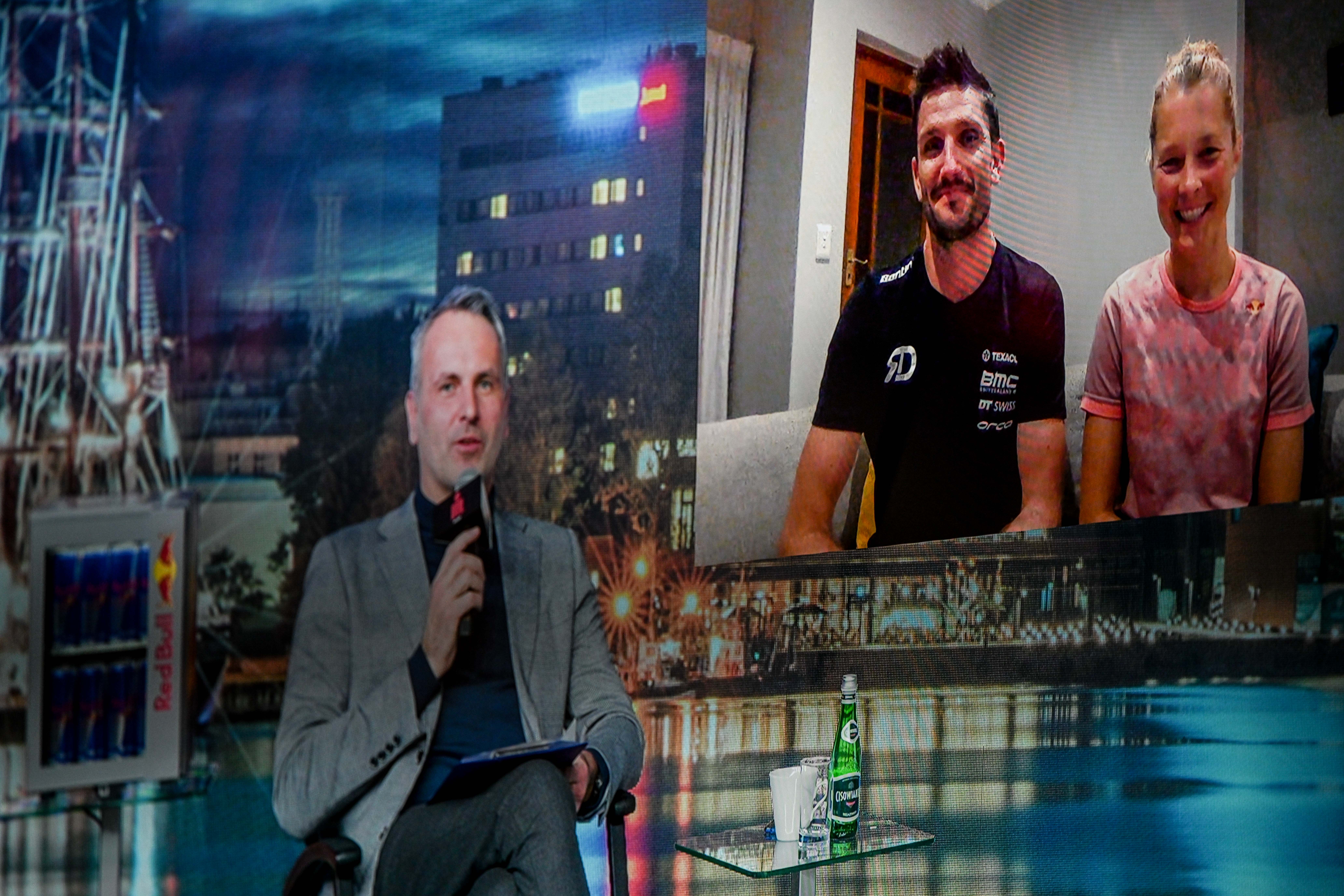 Na zdjęciu znajdują się prowadzący konferencję dziennikarz Jacek Kurowski, kt&oacute;ry siedzi na scenie oraz w mniejszym okienku małżeństwo triathlonist&oacute;w.