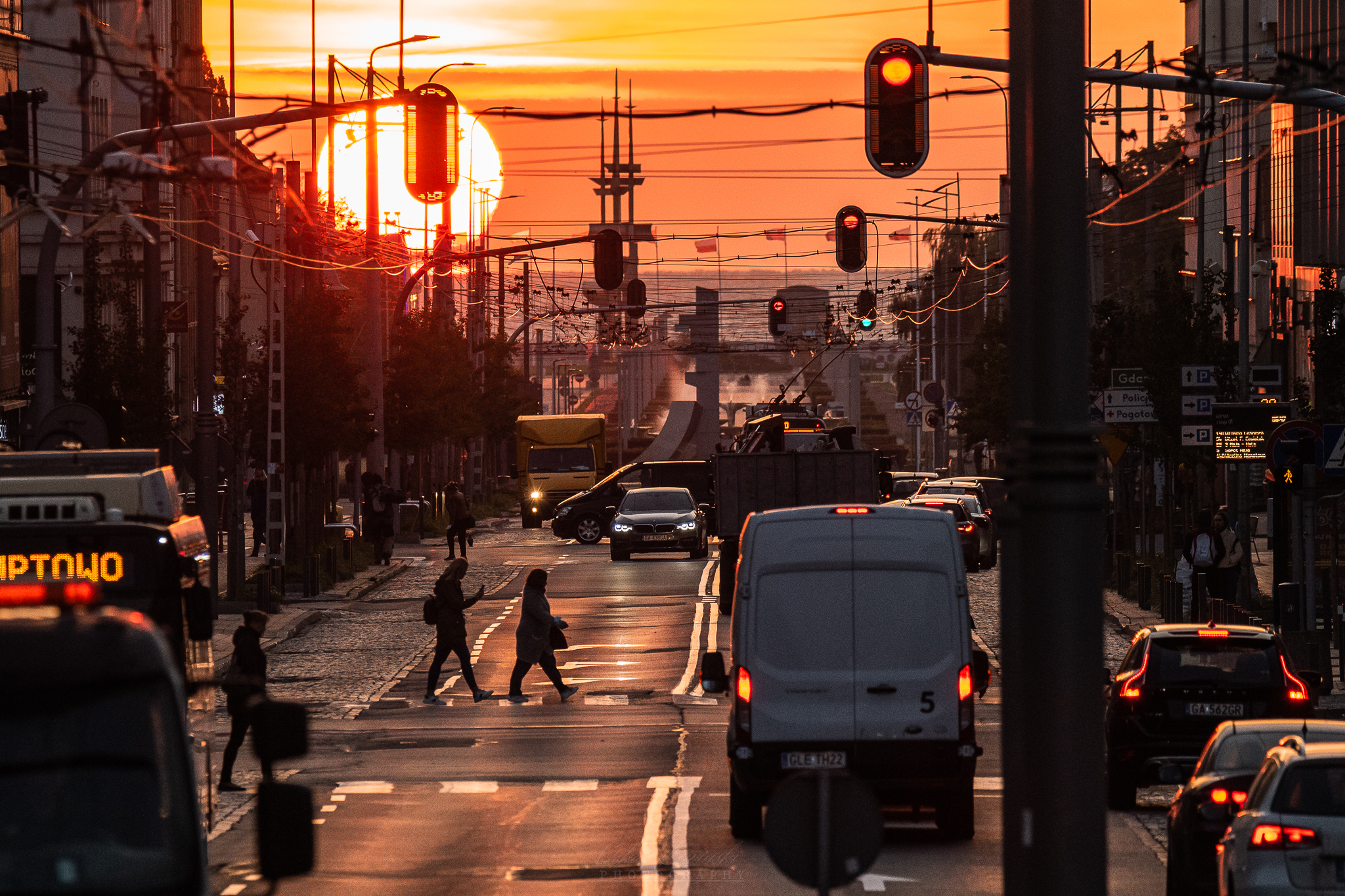 Ulica 10 Lutego w Gdyni, wsch&oacute;d słońca, samochody na jezdni, pieszy, budynki, pomnik w tle, morze