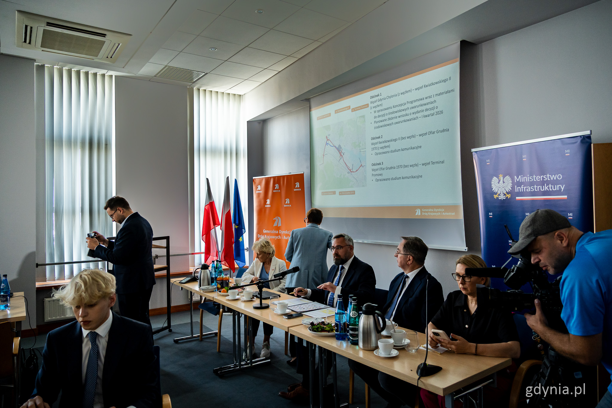 Sala konferencyjna w Porcie Gdynia, ludzie przy stołach, na ścianie ekran z wyświetlanym planem Drogi Czerwonej