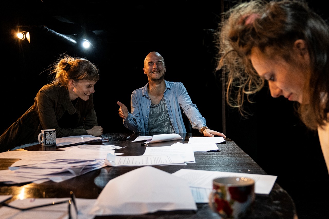 Troje aktor&oacute;w siedzi przy stole pełnym kartek