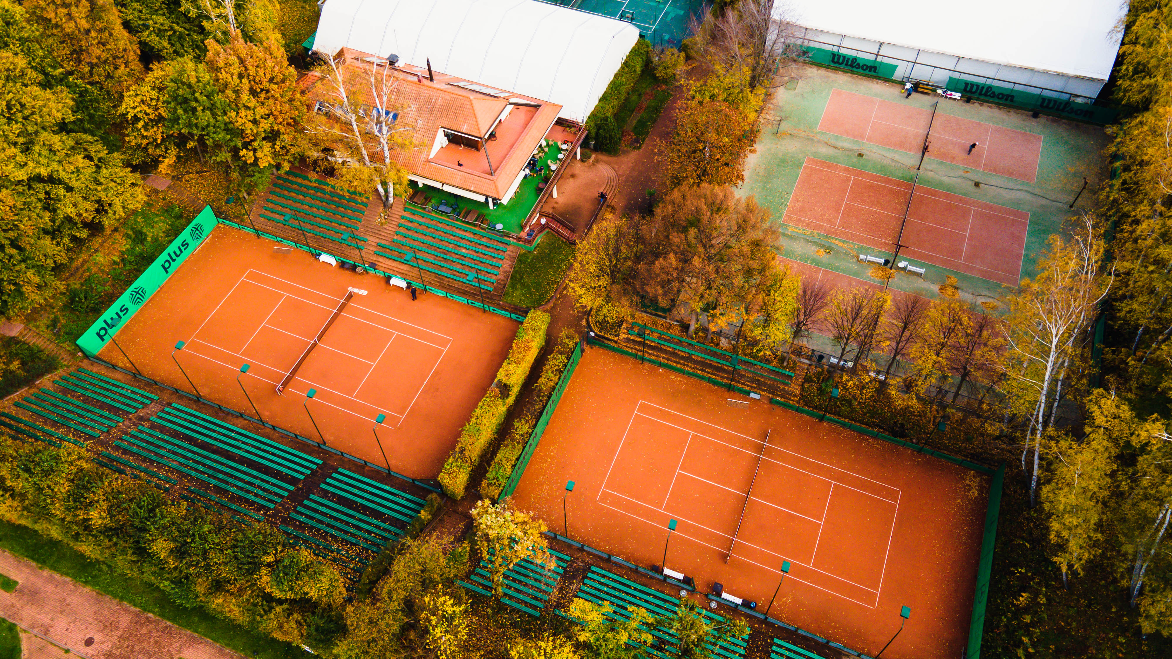 Korty tenisowe w Gdyni widziane z g&oacute;ry, widoczne zielone trybuny, pomarańczowa nawierzchnia, budynek obok