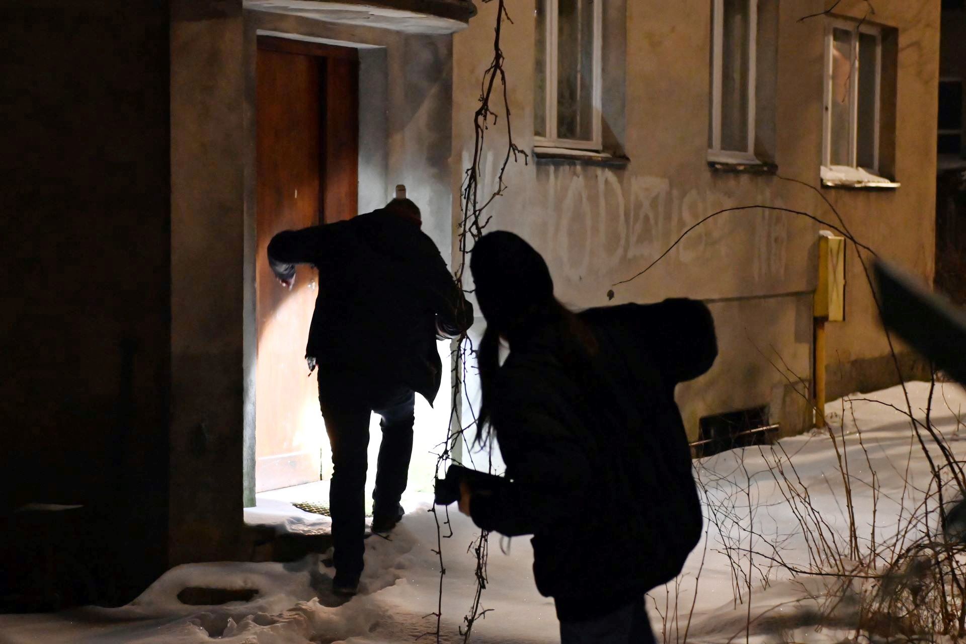 dwie osoby pr&oacute;bujące dostać się do zaśnieżonego pustostanu