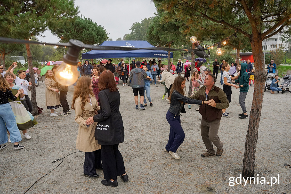Park Centralny, plac między drzewami, ludzie tańczą, w tle namioty, budynki, oświetlenie