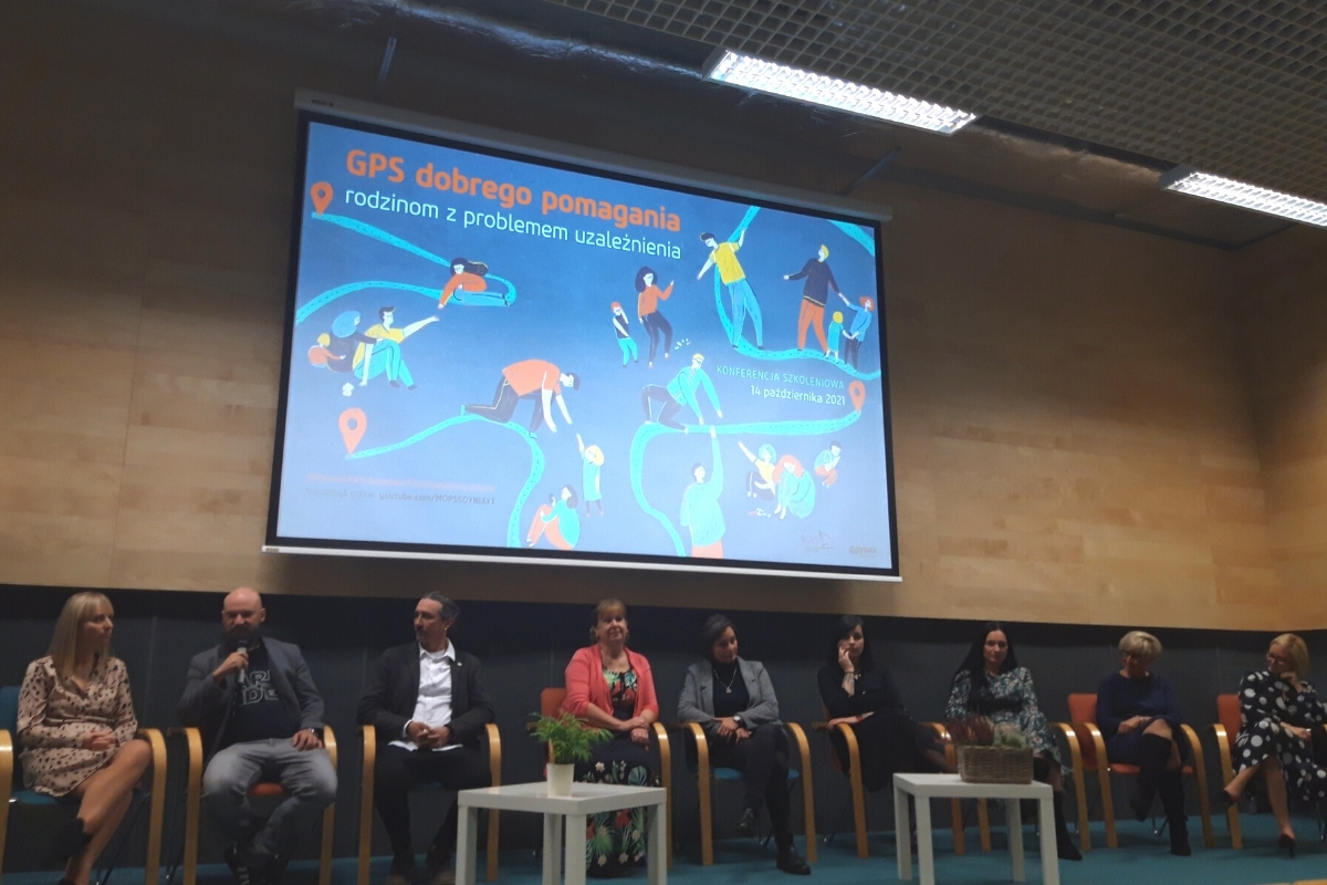 9 gości siedzi na podwyższeniu i rozmawia