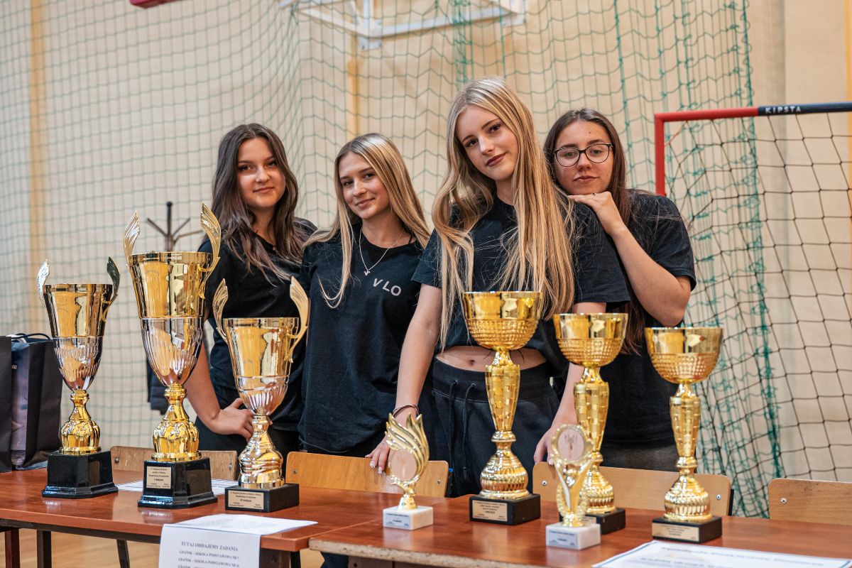 Uczennice w czarnych koszulkach stojące przy biurku z pucharami 