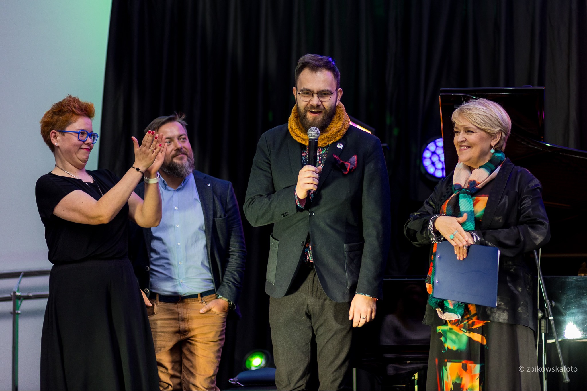 Wnętrze Muzeum Emigracji, grupa os&oacute;b przemawia przed publicznością, trzymają mikrofony