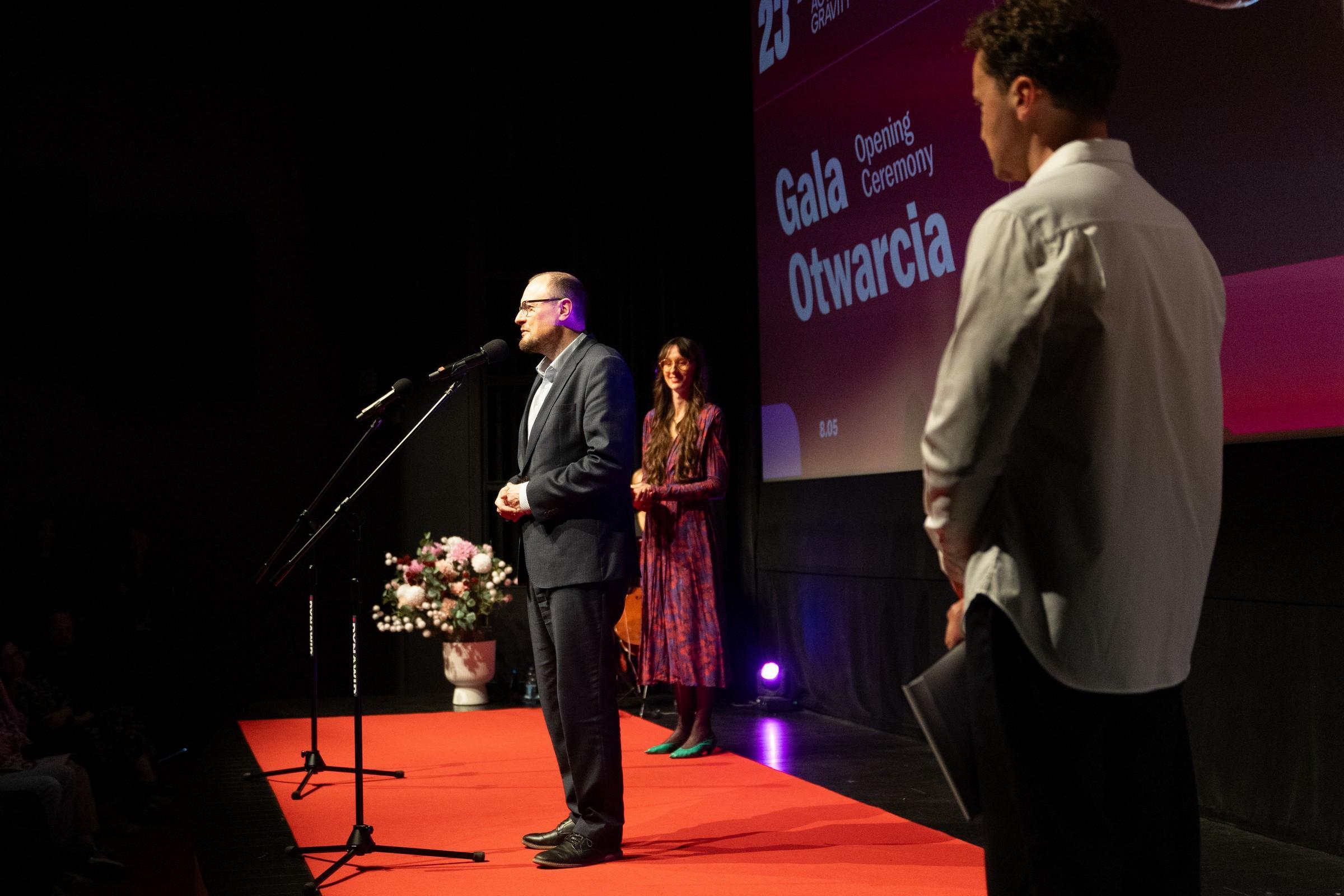 Mariusz Bzdęga, dyrektor zarządzający ds. kultury i aktywności mieszkańc&oacute;w, podczas gali otwarcia 23. Millennium Docs Against Gravity. Obok niego prowadzący wydarzenie Przemysław Rydzewski oraz Krystyna Weiher-Sitkiewicz (fot. Anna Rezulak)