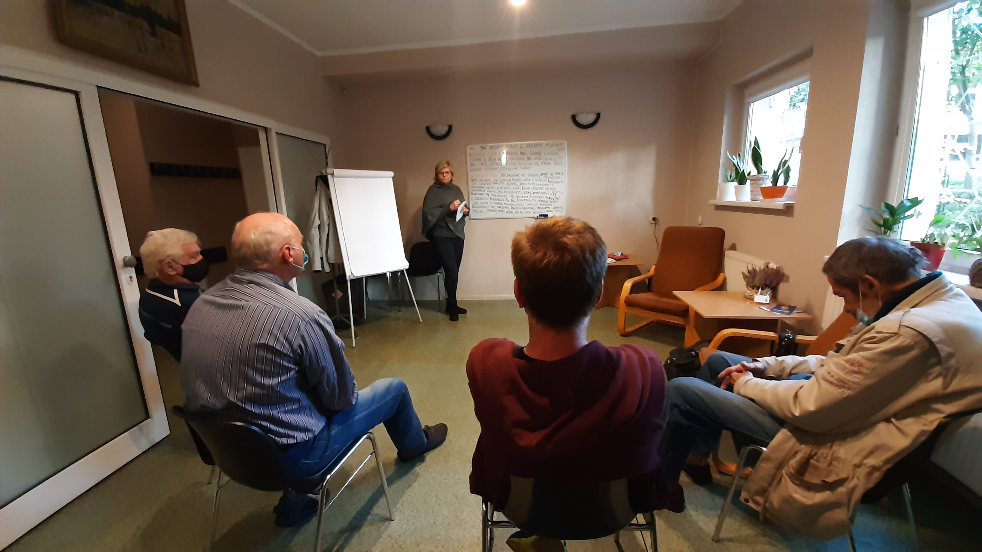 4 mężczyzn siedzi na krzesła, kobieta stoi przy tablicy