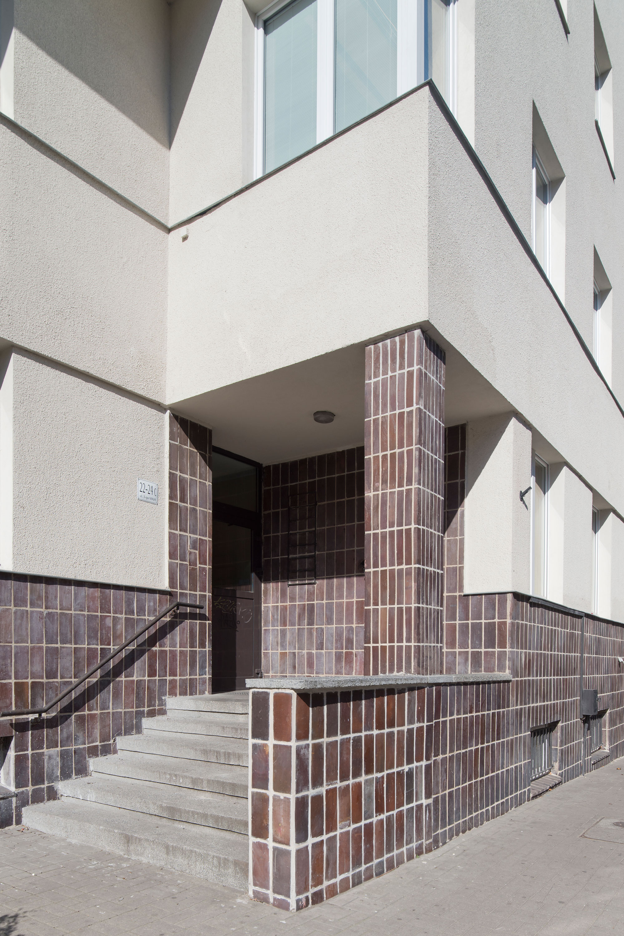 Strefa wejścia do budynku mieszkalnego ZUS przy ul. 3 Maja 22-24, brązowymi płytkami oblicowano ściany w podcieniu i cok&oacute;ł.