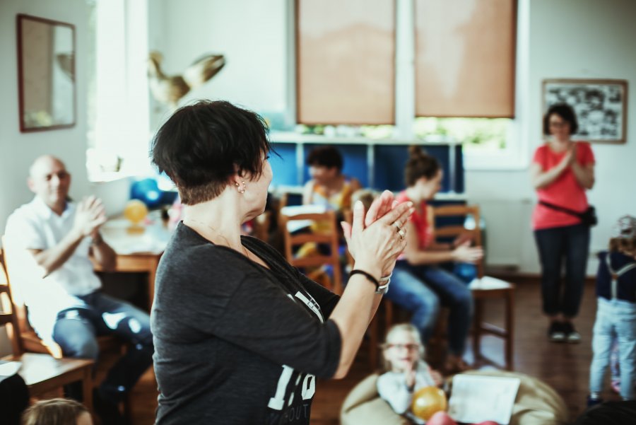 Kobieta klaszcząca w dłonie, w tle uczestnicy zajęć