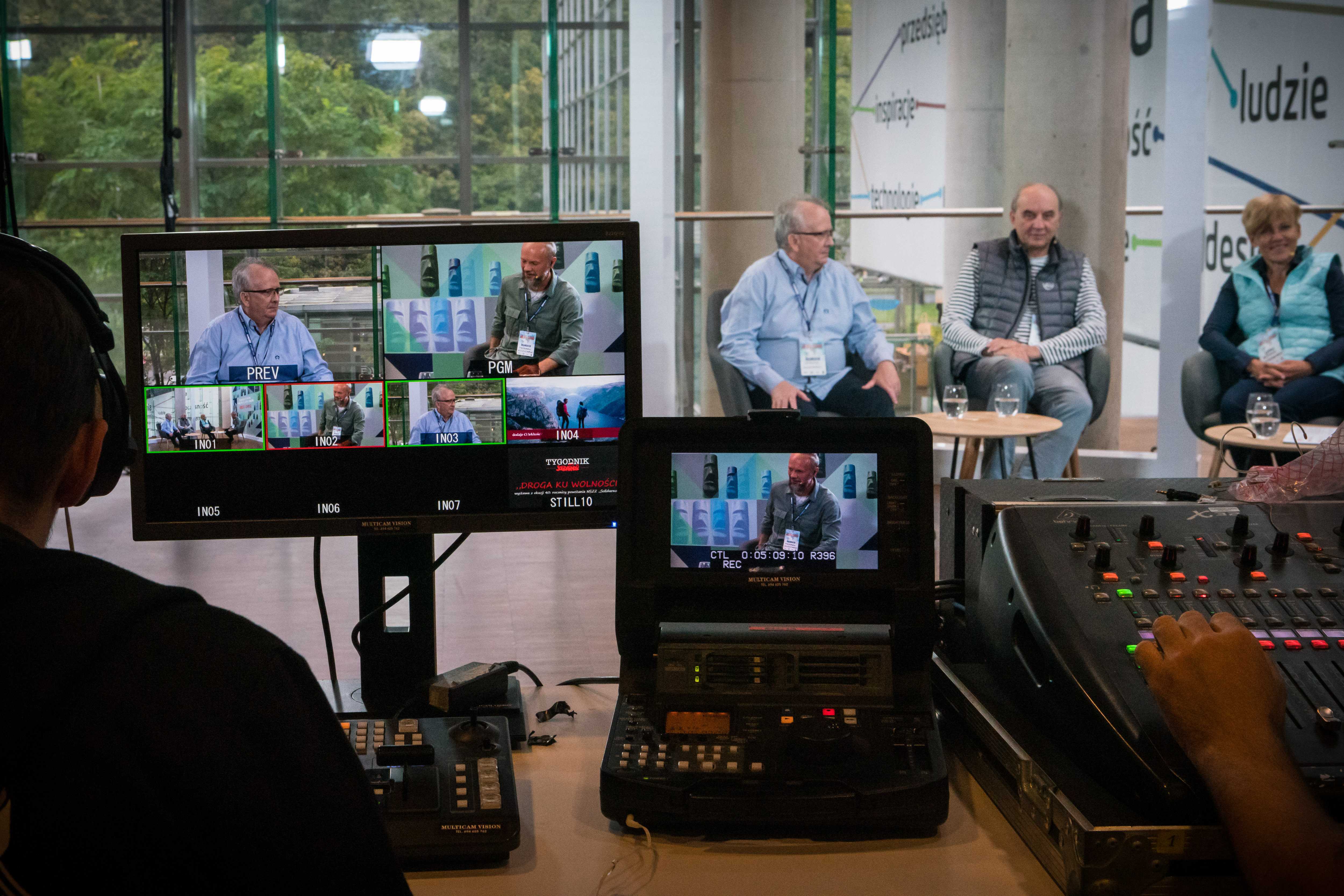 Studio Kolos&oacute;w. Na pierwszym planie monitory, na kt&oacute;rych widać podgląd transmisji. W poszczeg&oacute;lnych okienkach widoczni są rozm&oacute;wcy. W tle goście studia siedzą w fotelach // fot. Anna Rezulak