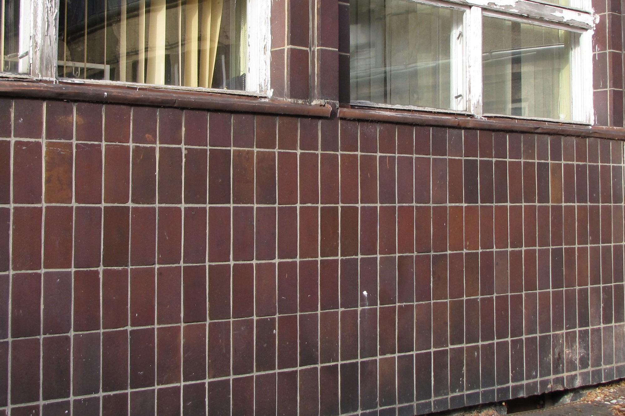 Fragment cokołu budynku na Grabówku oblicowany brązowymi płytkami z jasnymi spoinami.